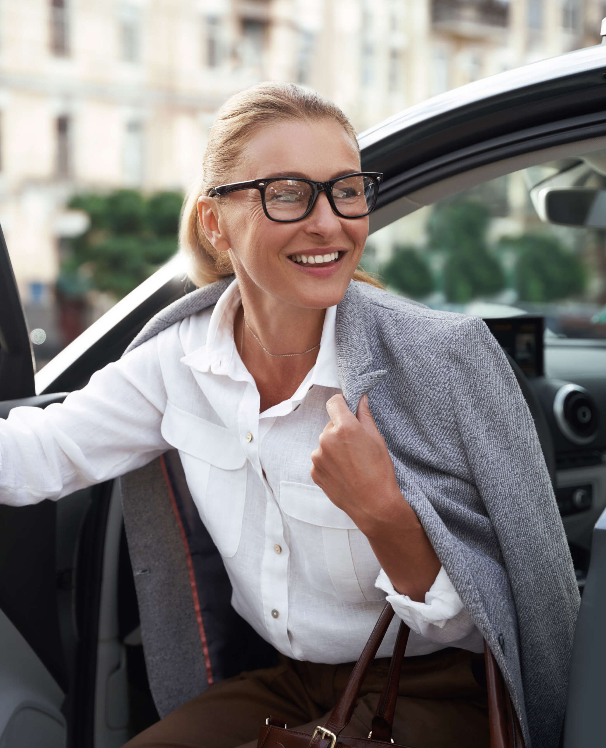 Attractive happy business woman in classic wear getting out of her modern car and smiling